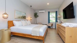 A modern bedroom with a wooden bed, bedside tables, a TV, and a window with curtains. - Magnolia Deluxe King Studio at The Dogwood (Maggie Valley)