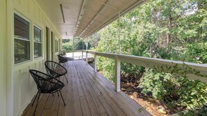 A covered porch with a wooden floor, metal chairs, and a railing overlooking a wooded area. - Magnolia Deluxe King Studio at The Dogwood (Maggie Valley)