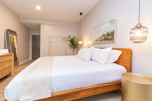 Un dormitorio con cama de madera, mesita de noche, espejo, lámpara colgante y un cuadro en la pared.