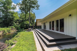 A modern house with a deck, a small garden, and a stream.