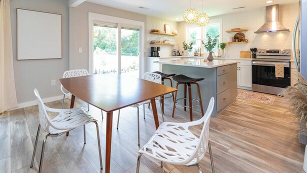 A modern kitchen with a central island, stainless steel appliances, and a dining area with white chairs. - Chic Creekside Bungalow at The Dogwood (Maggie Valley)