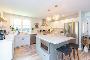 A modern kitchen with white cabinetry, stainless steel appliances, and a large island with bar stools.