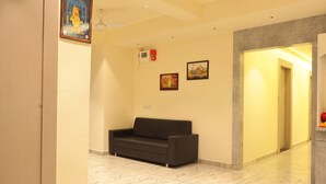 A reception area with a dark-colored sofa, a framed picture on the wall, and a tiled floor. - Hotel NS Residency (Ahmedabad)