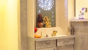 A bathroom with a marble sink, a mirror, and a shelf with a phone and a small statue. - Hotel NS Residency (Ahmedabad)