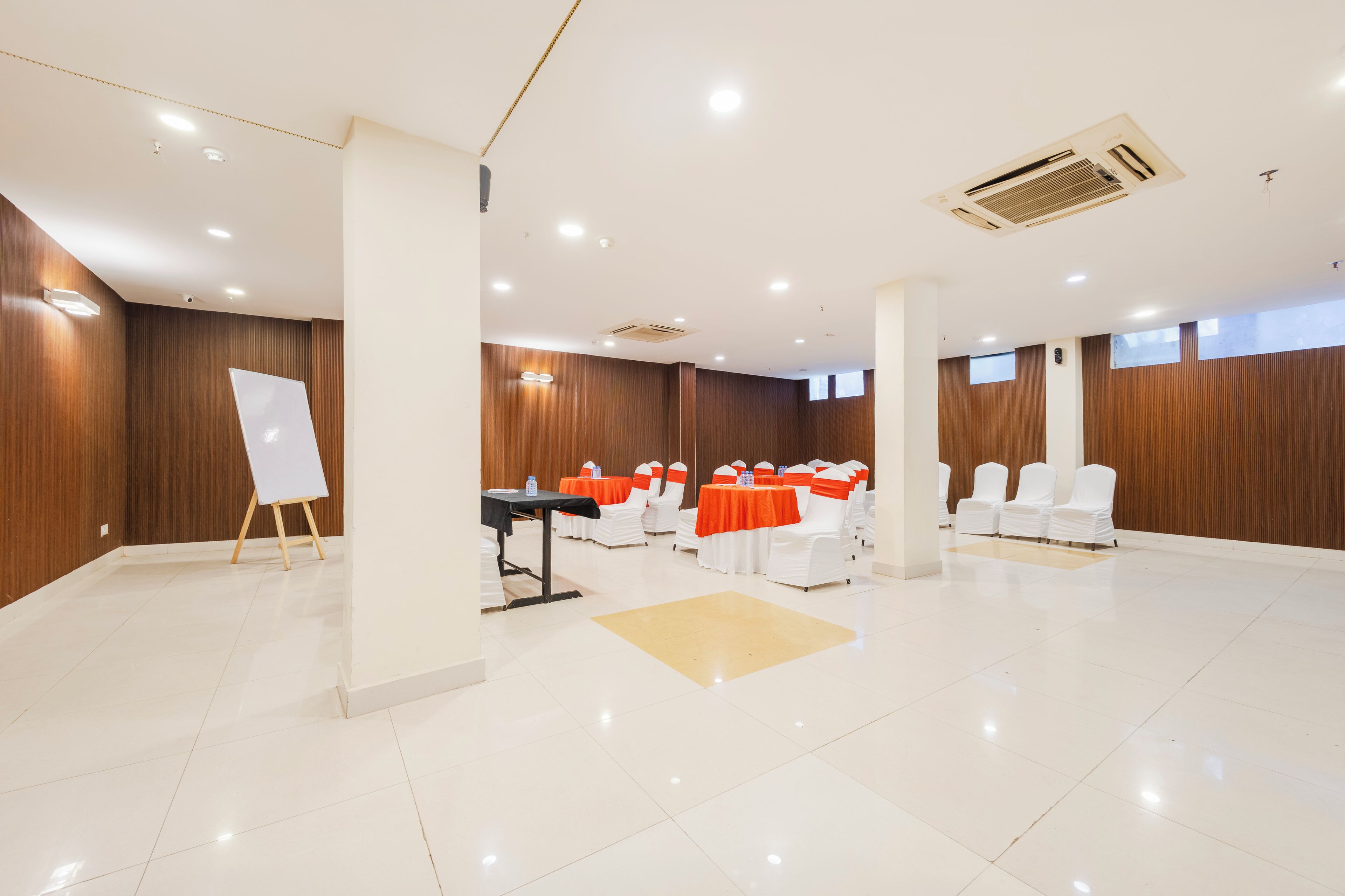 Une salle de conférence spacieuse, dotée de chaises blanches, d’un tableau blanc et de tables recouvertes de nappes orange.