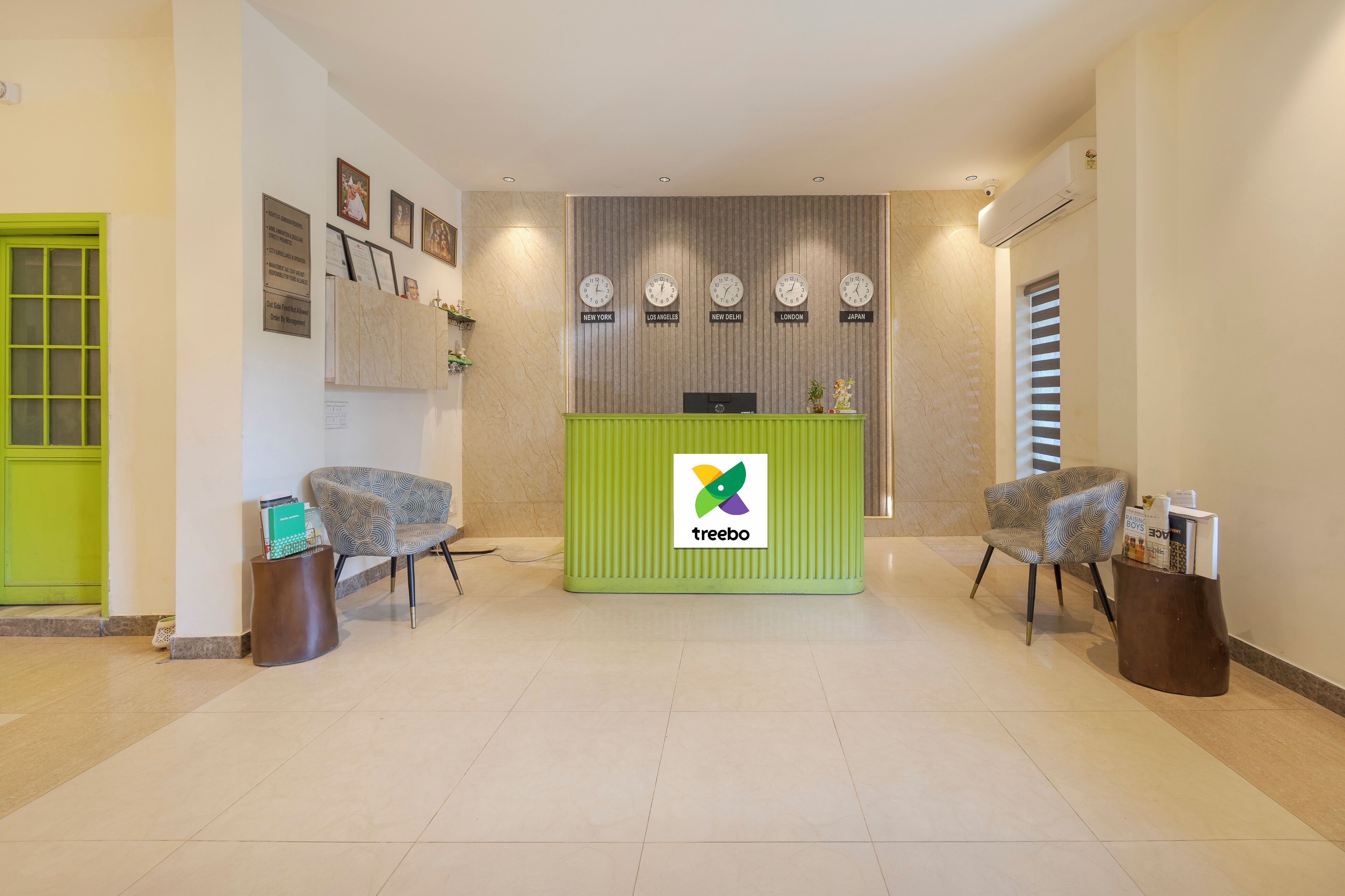 A reception area with a green desk, two patterned chairs, a clock wall, and a green door.