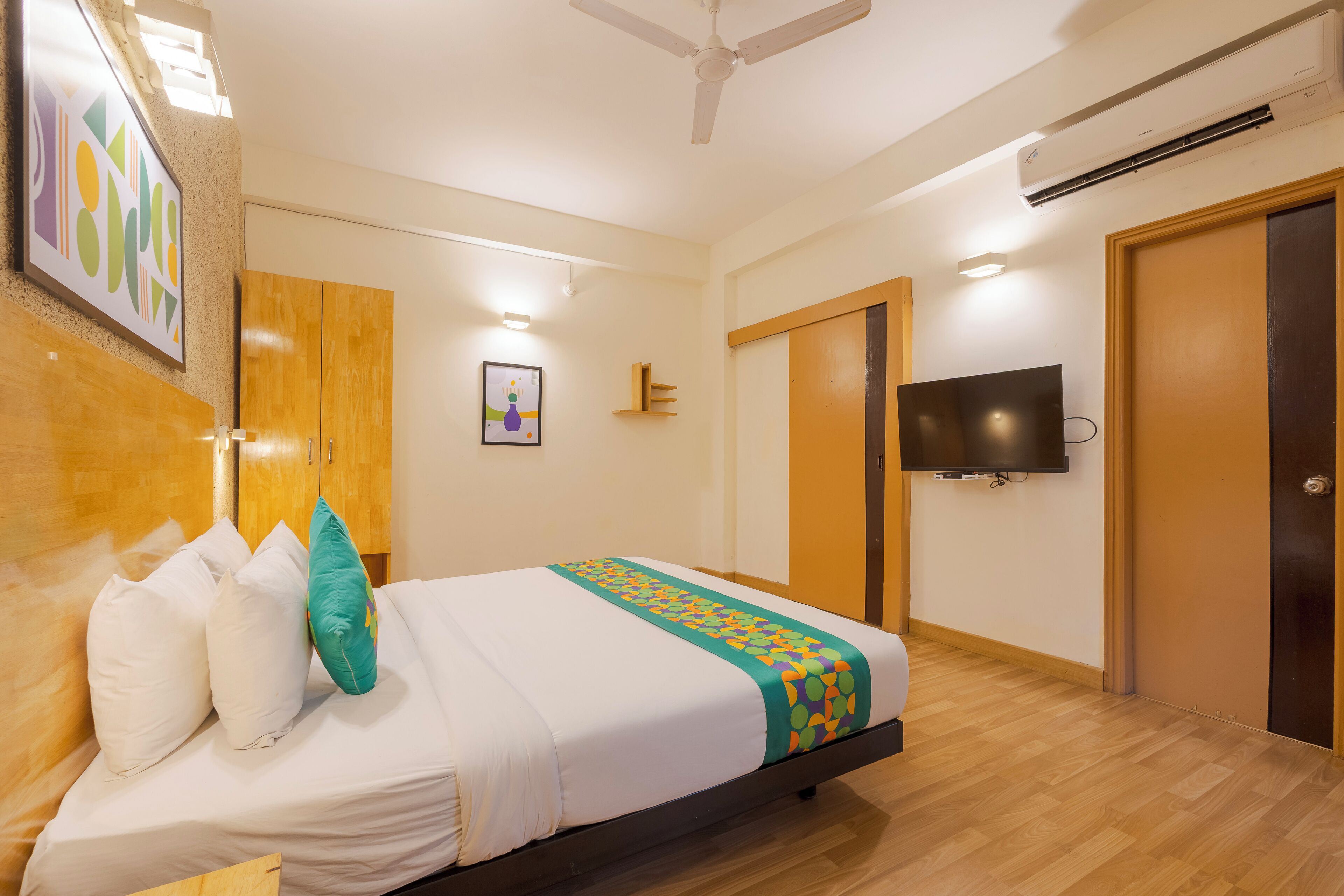 A hotel room with a bed, a TV mounted on the wall, and a wooden wardrobe.
