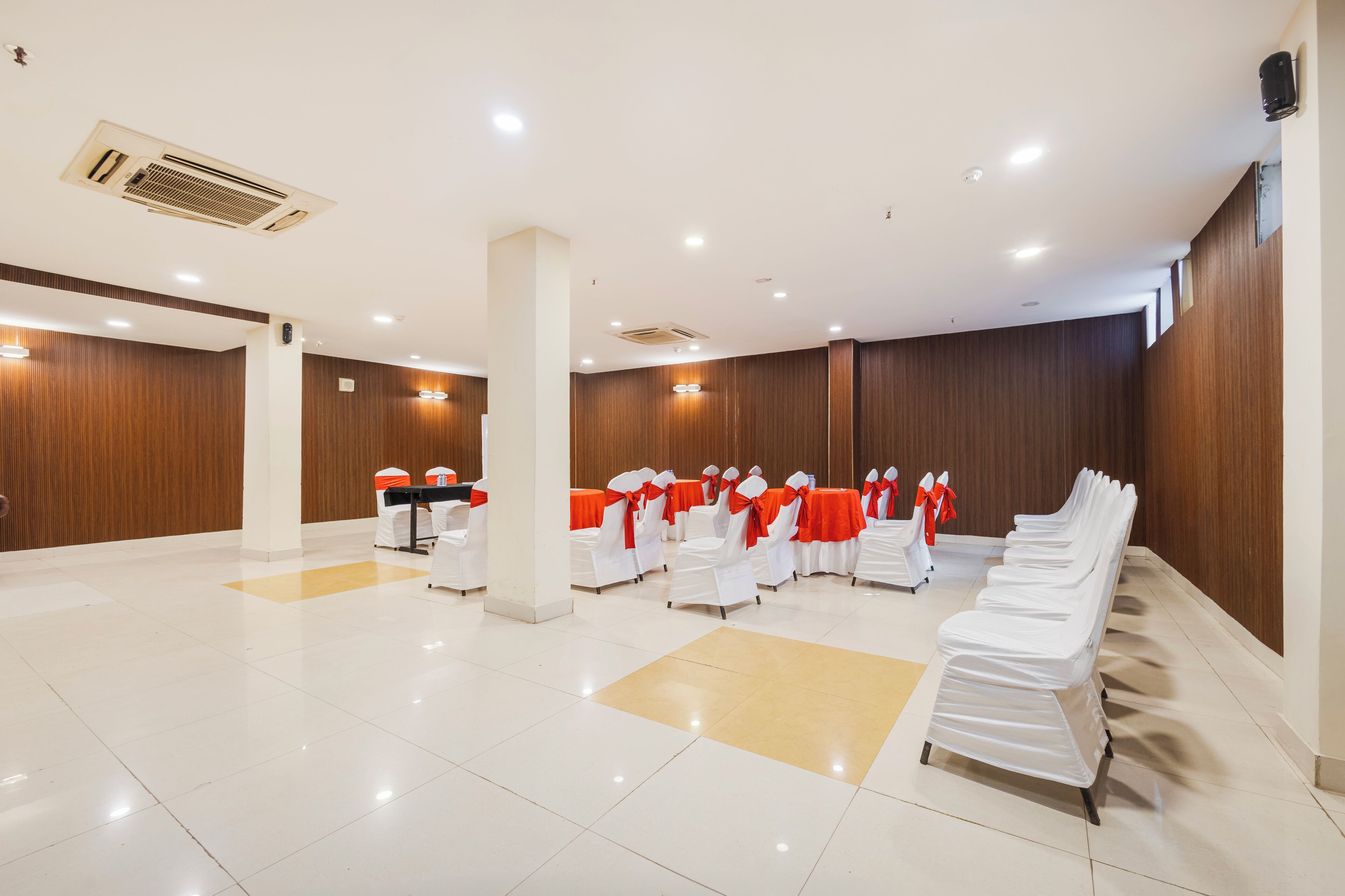 A spacious hall with rows of white chairs, some with red sashes, and tables with white tablecloths.