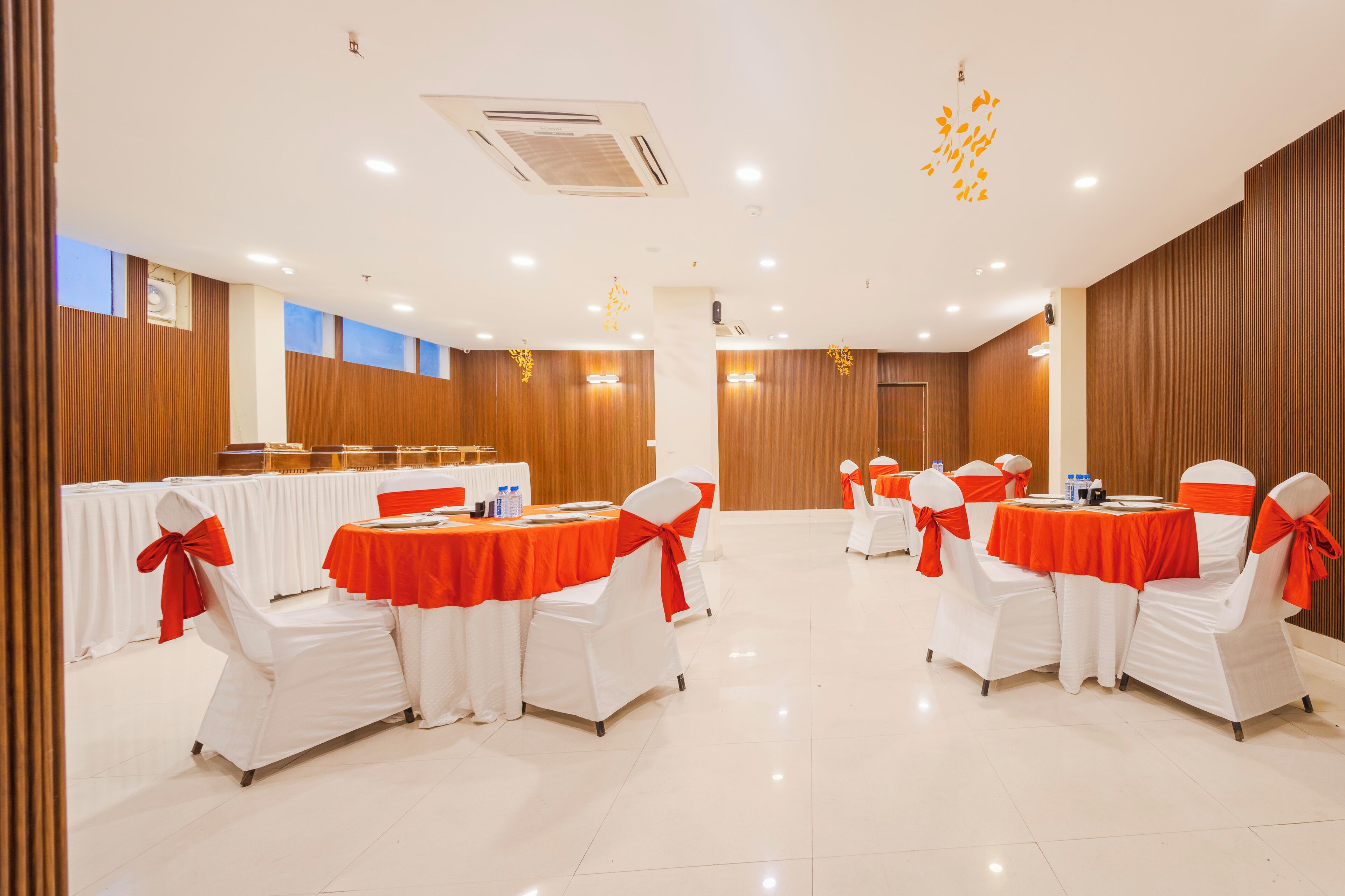 A conference room with white chairs and tables, each with a red bow. The room has wooden paneling and a white ceiling with recessed lighting.