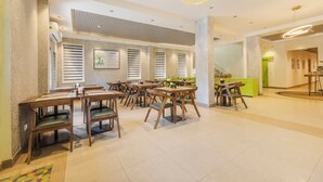 A spacious dining area with multiple wooden tables and chairs, a modern ceiling design, and a green reception desk. - Treebo Ace Luxe (New Delhi)