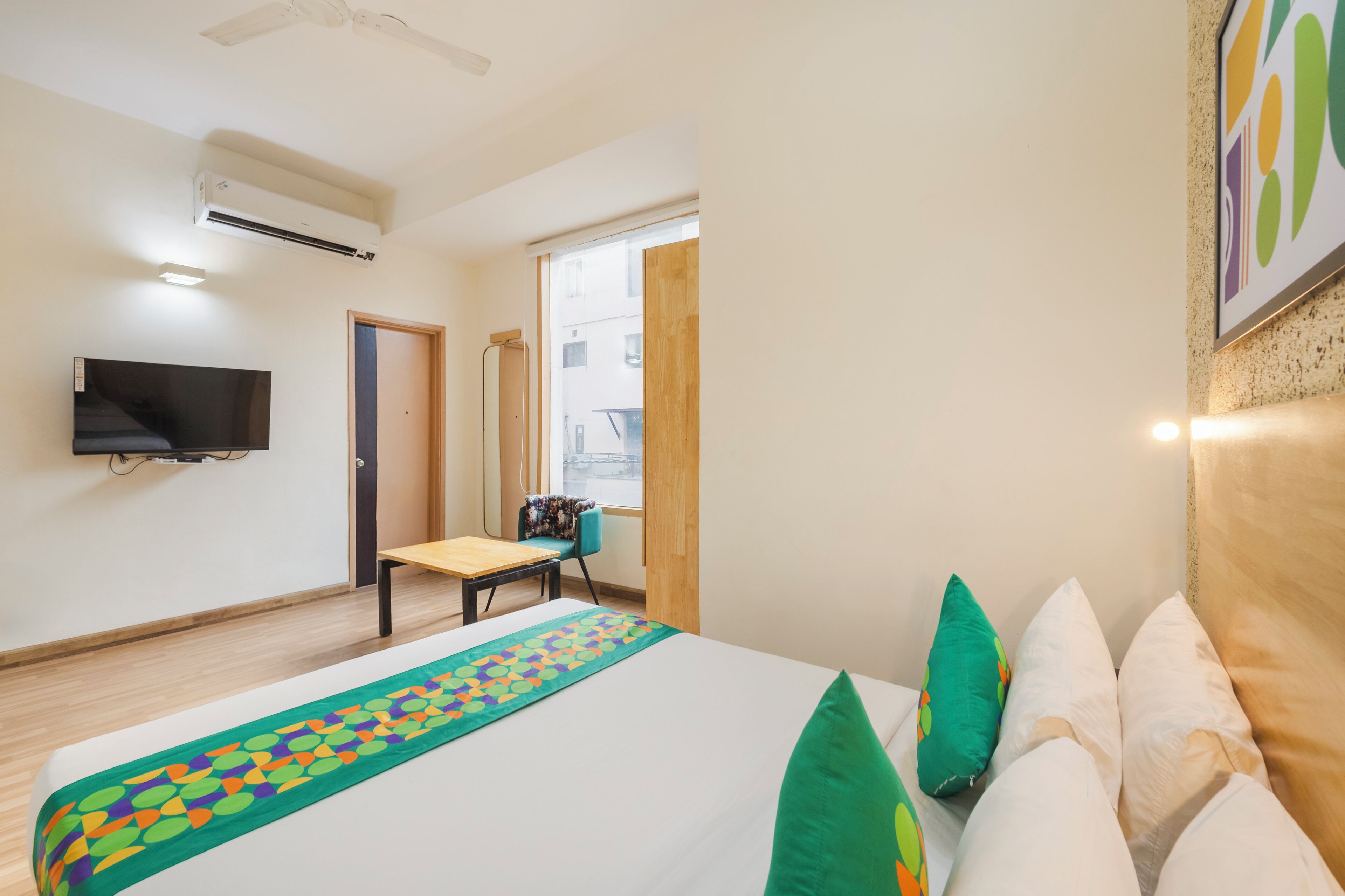 Una habitación de hotel con una cama, un televisor montado en la pared, un escritorio y una silla.