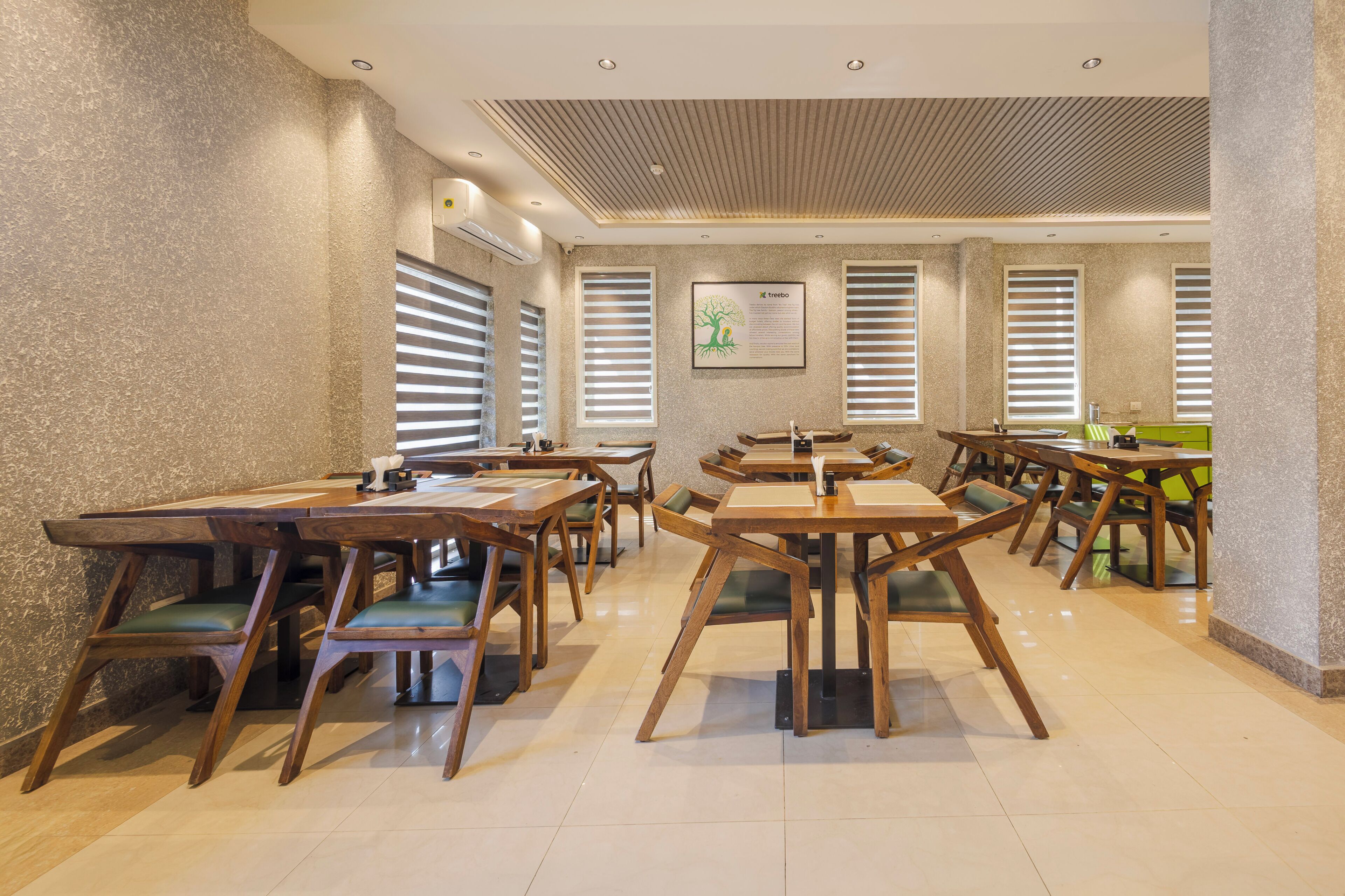 A spacious dining area with multiple wooden tables and chairs, large windows with blinds, and a ceiling with recessed lighting.