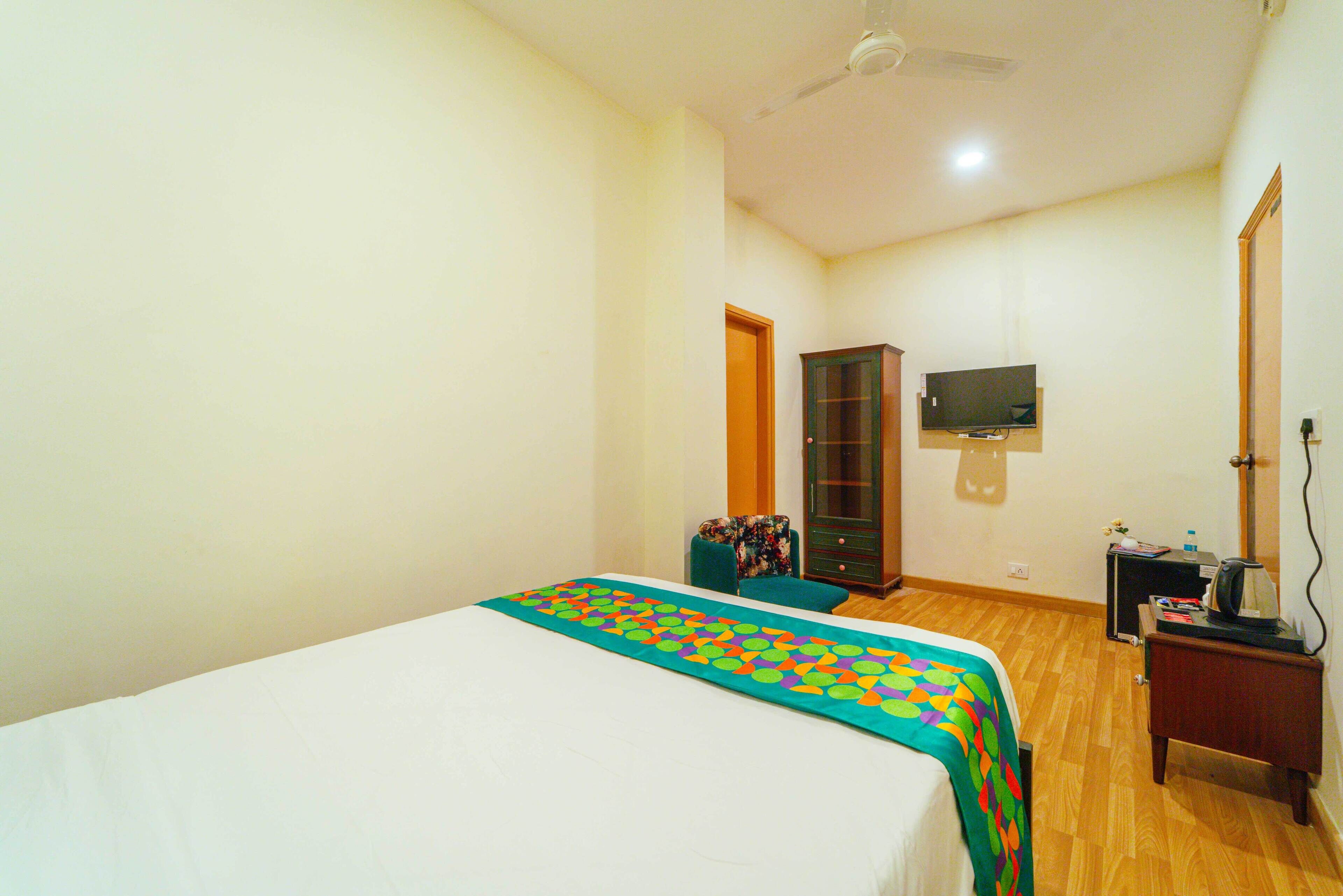A bedroom with a bed, a television mounted on the wall, a cabinet, and a desk with a kettle.