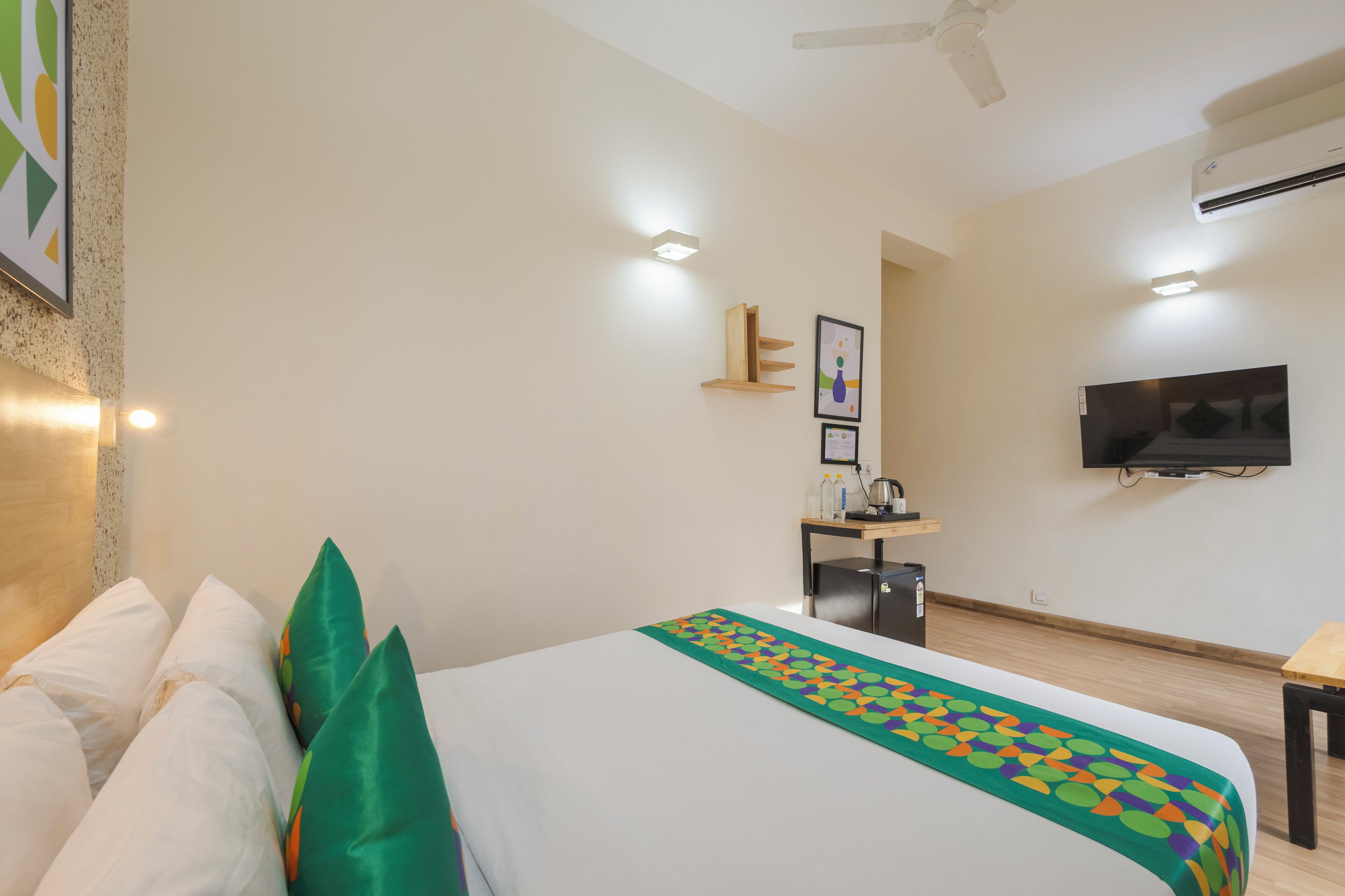 A hotel room with a bed, a desk, a chair, a TV, and an air conditioning unit.