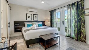 A modern bedroom with a large bed, a bedside table, a ceiling fan, and a view of the outdoors through a sliding door.