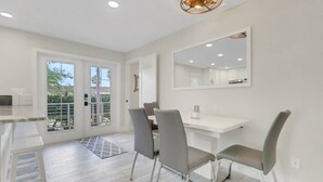 A modern kitchen with white cabinetry, a large window, and a dining area with grey chairs and a white table.