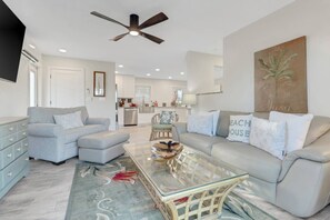 A modern living room with a grey sofa, a glass coffee table, and a ceiling fan. - Private Pool & Spa Retreat! Walk to the Beach | Beautifully Remodeled 1st Floor Mid-Island Apartment (Fort Myers Beach)