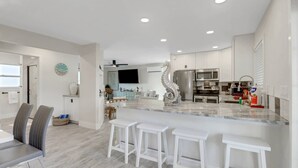 A modern kitchen with white cabinetry, a marble island, and a stainless steel refrigerator.