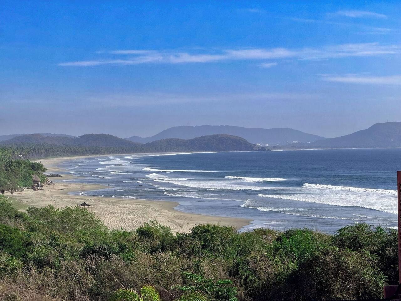 Un paysage côtier avec une plage, des vagues de l’océan et des collines à l’horizon.