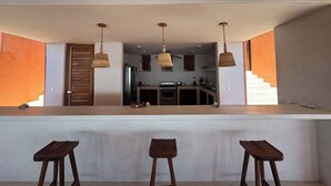 A modern kitchen with a central island, pendant lighting, and a view of the living area. - Luxury Eco in Troncones Casa Mia (Troncones)
