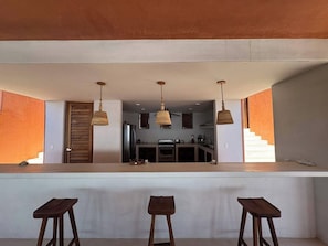 Una cucina moderna con isola centrale, illuminazione a sospensione e vista sull'area living.