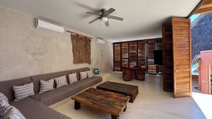 A modern living room with a sofa, two coffee tables, a ceiling fan, and a large window with blinds. - Luxury Eco in Troncones Casa Mia (Troncones)