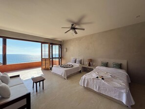 A hotel room with two beds, a ceiling fan, and a view of the ocean.