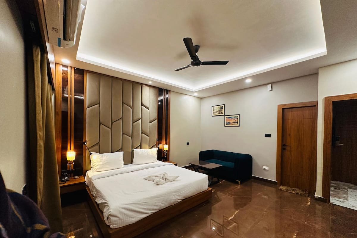Habitación de hotel moderna con una cama grande, ventilador de techo, escritorio y sofá azul.