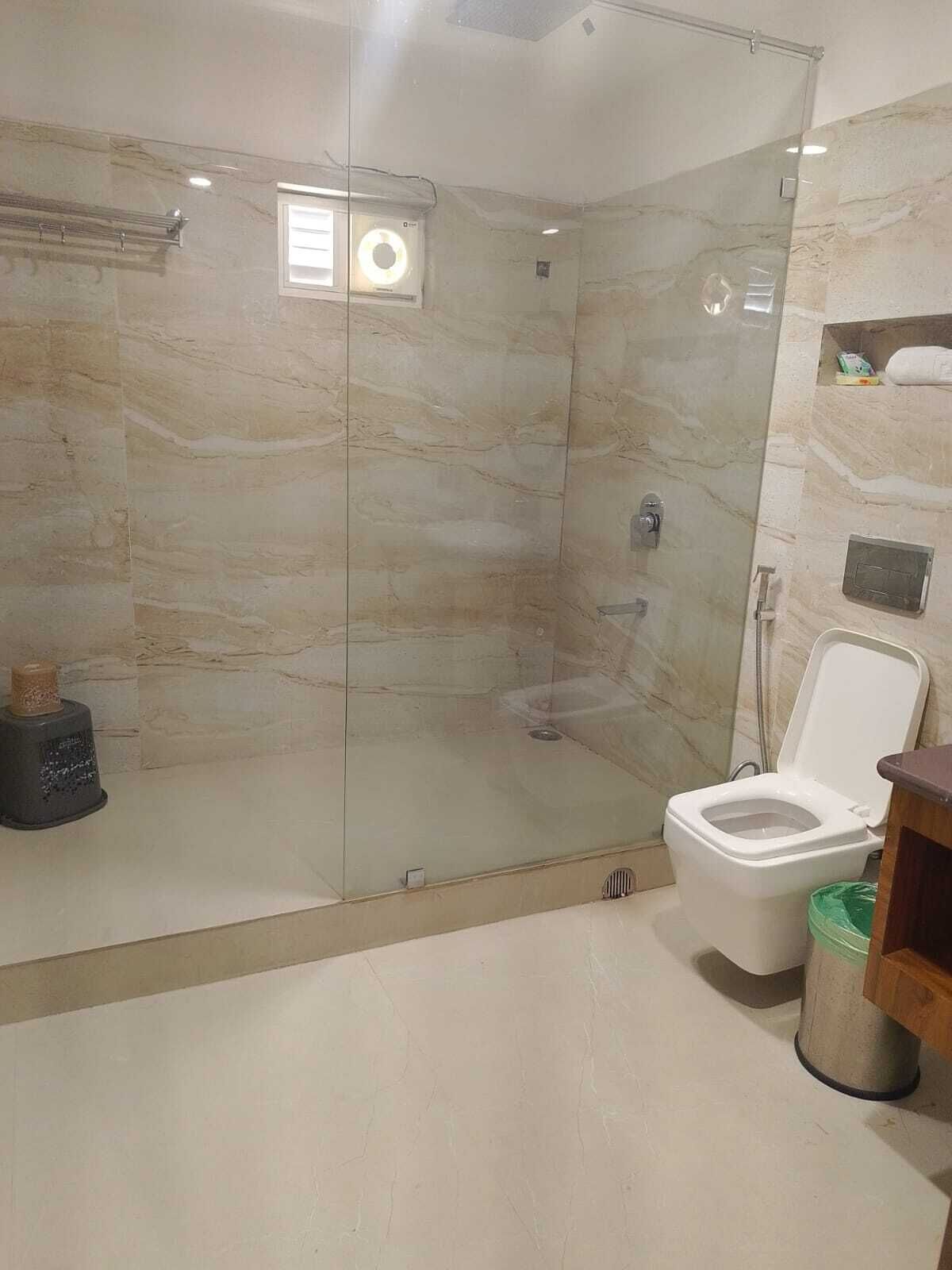 A modern bathroom with a glass-enclosed shower, a toilet, and a trash bin.