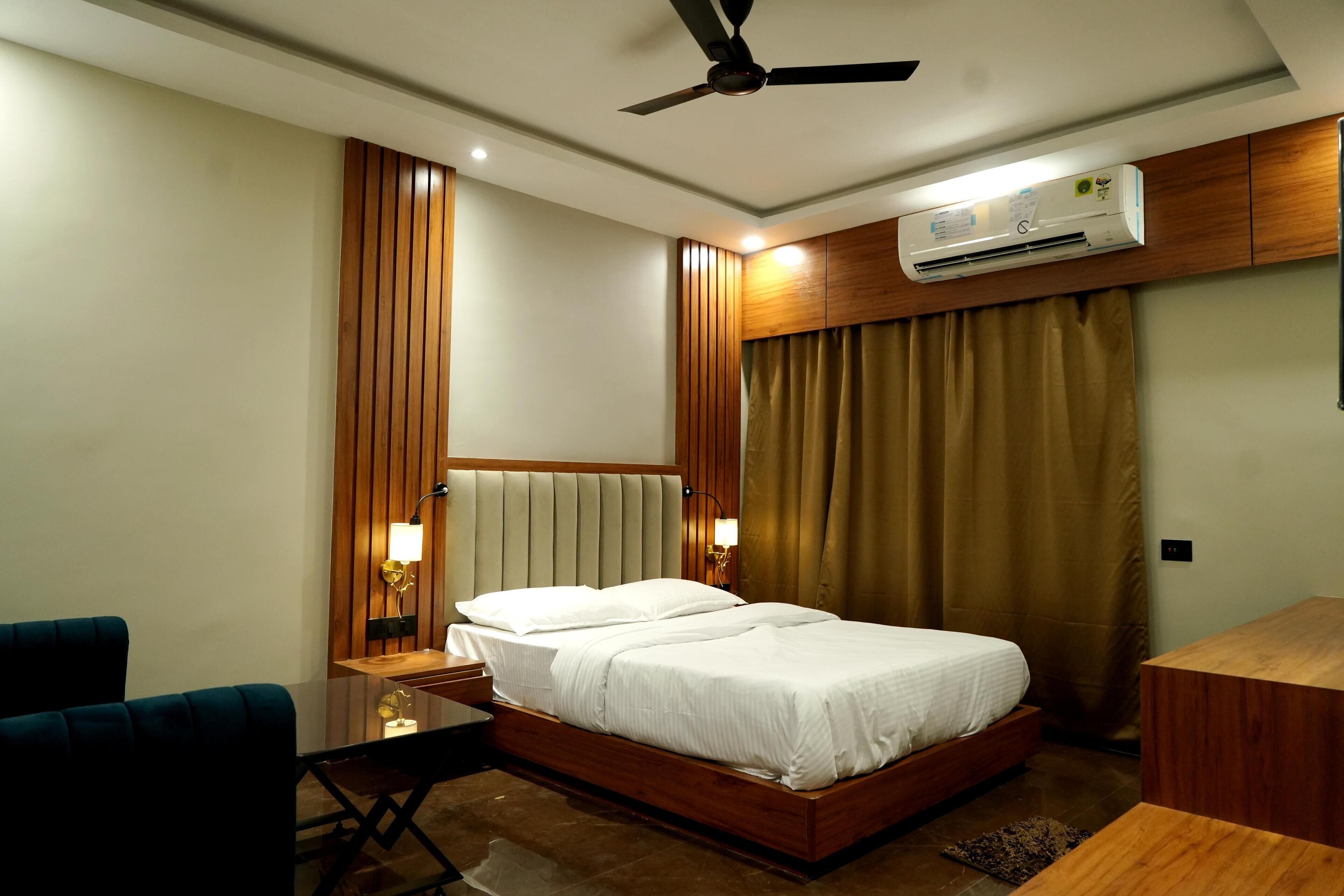 Habitación de hotel con cama, escritorio, silla, equipo de aire acondicionado y ventilador de techo.