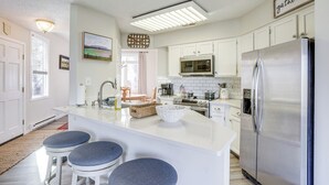 Eine moderne Küche mit weißen Schränken, einem Edelstahlkühlschrank, einer Mikrowelle und einer großen Kochinsel mit Barhocker.