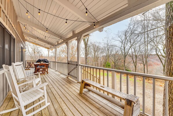 A wooden deck with string lights, a bench, and a table with chairs. - 5 Mi to Beaver Lake: Family Cabin w/ Game Room (Eureka Springs)