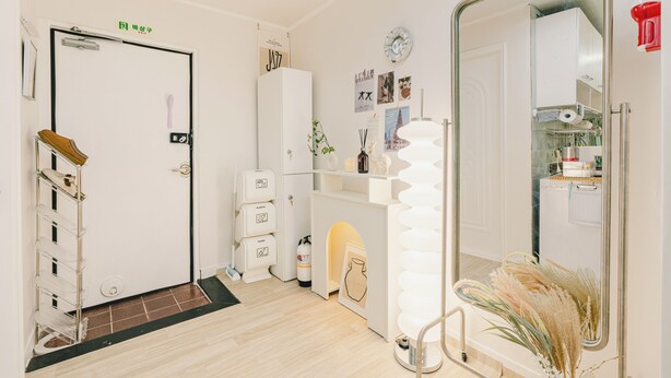 A compact, well-organized room with a white door, a small kitchenette, a mirror, and a door with a green sign.