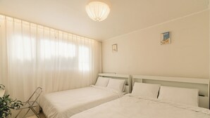 A hotel room with two beds, a bedside table, a lamp, and a plant.