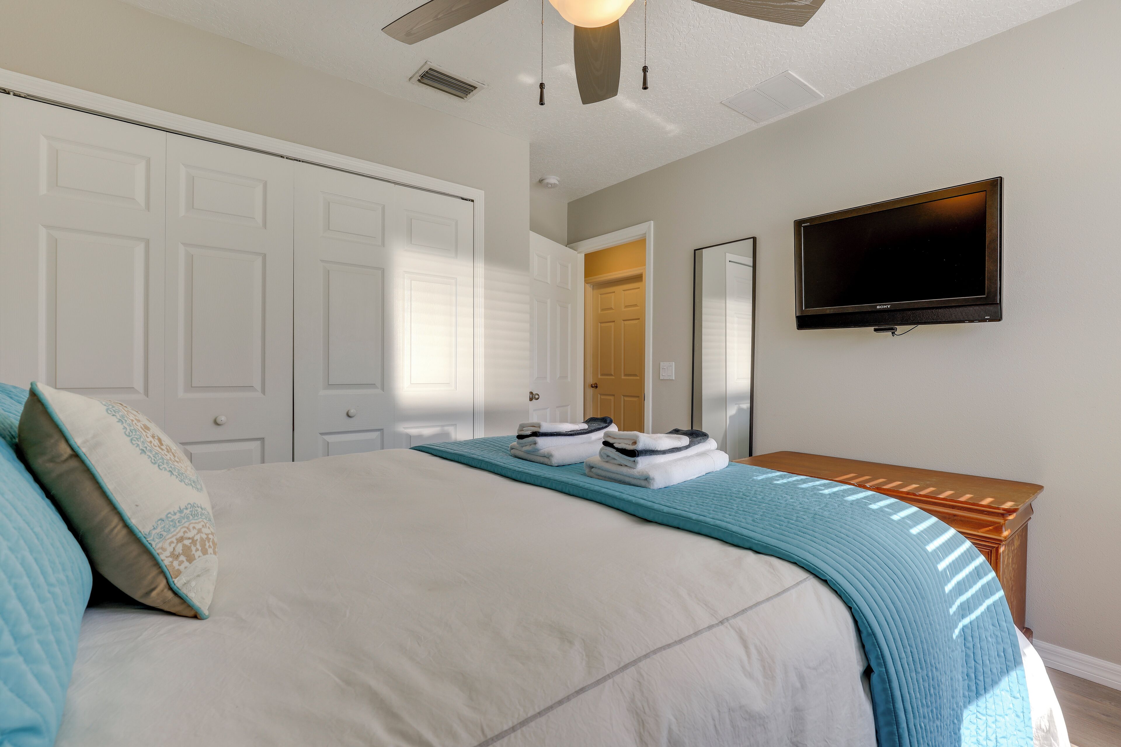 A bedroom with a bed, a ceiling fan, a TV mounted on the wall, and a wooden nightstand.