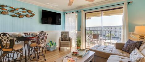A spacious living room with a ceiling fan, a dining area with chairs and a table, a sofa, and a view of the outdoors through a sliding glass door.
