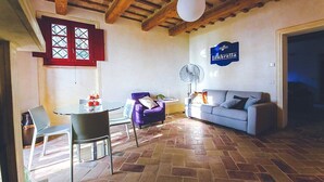 A living room with a stone floor, a sofa, a purple armchair, a table with chairs, and a fan.