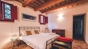 A bedroom with a bed, a nightstand, a lamp, a wooden cabinet, and a suitcase.