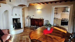 Un comedor con mesa de madera, sillas, chimenea y cocina al fondo.