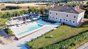 Una casa grande con piscina, un porche cubierto y un césped bien cuidado.