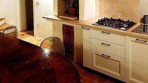 Una cocina con estufa a gas, armarios blancos, techo de madera y un pequeño respiradero.