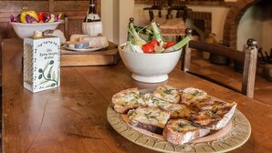 Una mesa de madera con un plato de pan tostado adornado con hierbas, un bol de ensalada y un recipiente de aceite de oliva virgen extra.