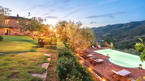 Una casa de piedra con piscina, rodeada de un jardín cuidado y vistas a las colinas.