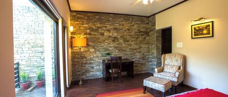 A bedroom with a stone wall, a ceiling fan, a chair, a bed, and a view of the outside.