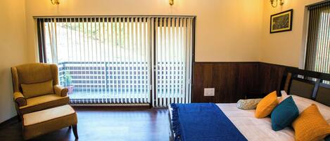A room with a bed, a chair, and a view through a window with blinds.
