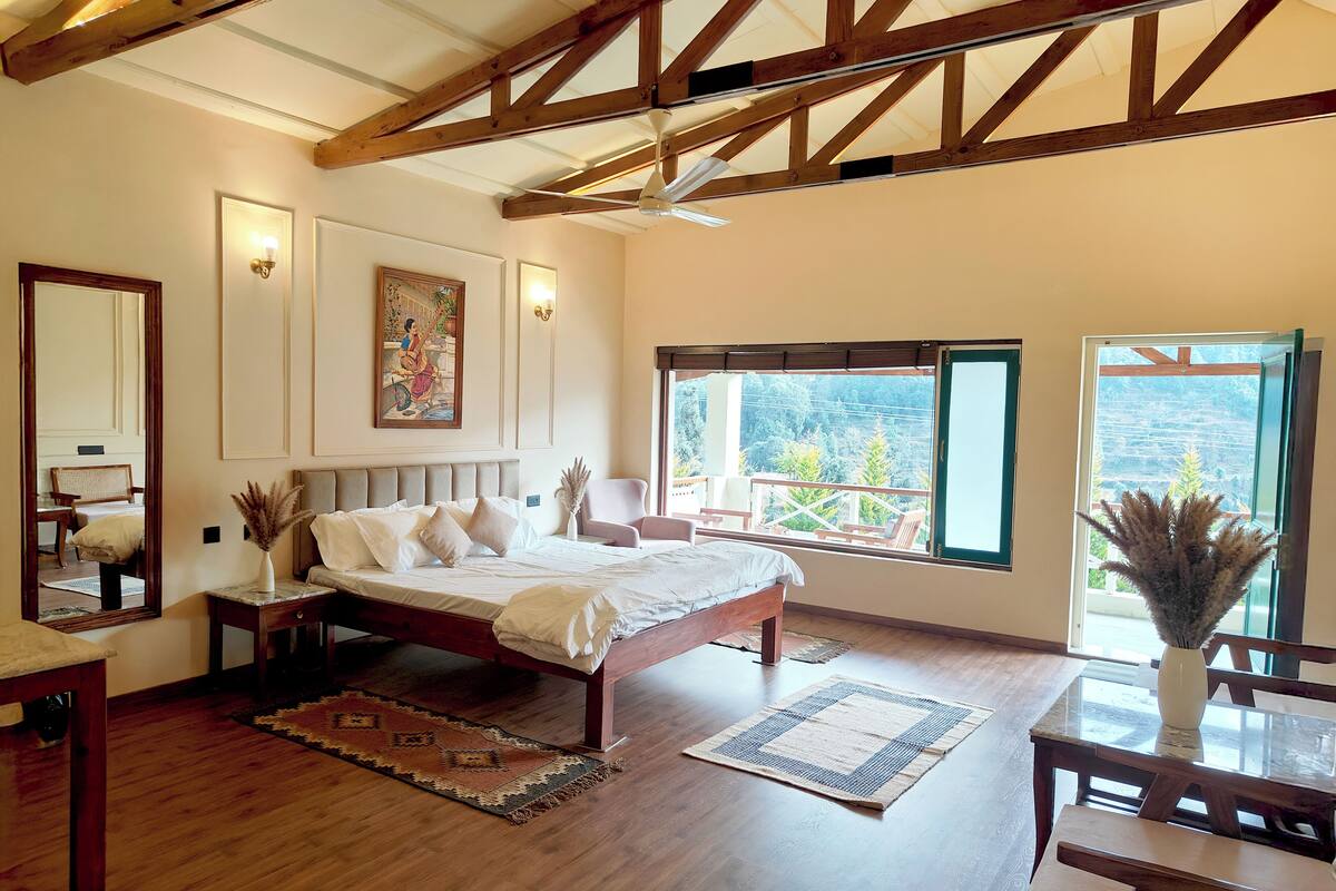 Un dormitorio amplio con una cama grande, una zona de estar con mesa y sillas, y un balcón con vistas al exterior.