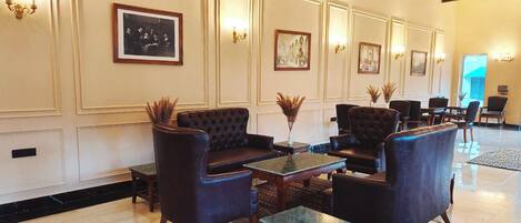 A lobby with a black leather sofa, armchairs, and a coffee table. There are framed pictures on the walls and a chandelier.