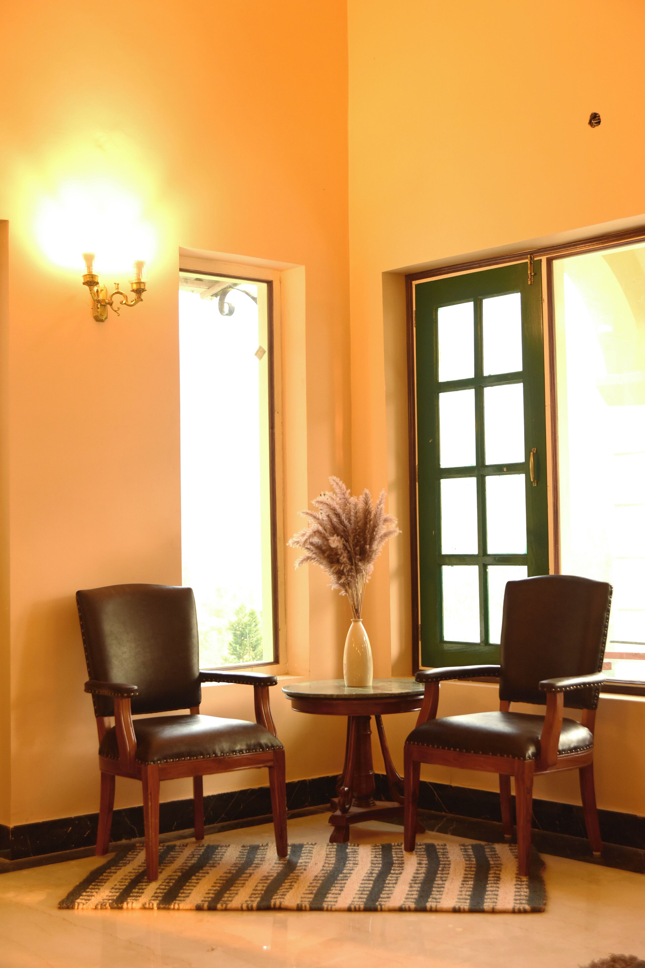 A room with two leather chairs, a small table, a vase with dried plants, and a green door with a window.