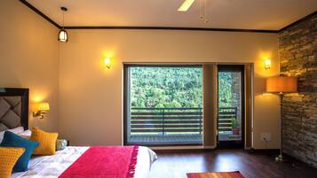 Un dormitorio con una cama grande, piso de madera, balcón con vistas a la vegetación y una pared de piedra.