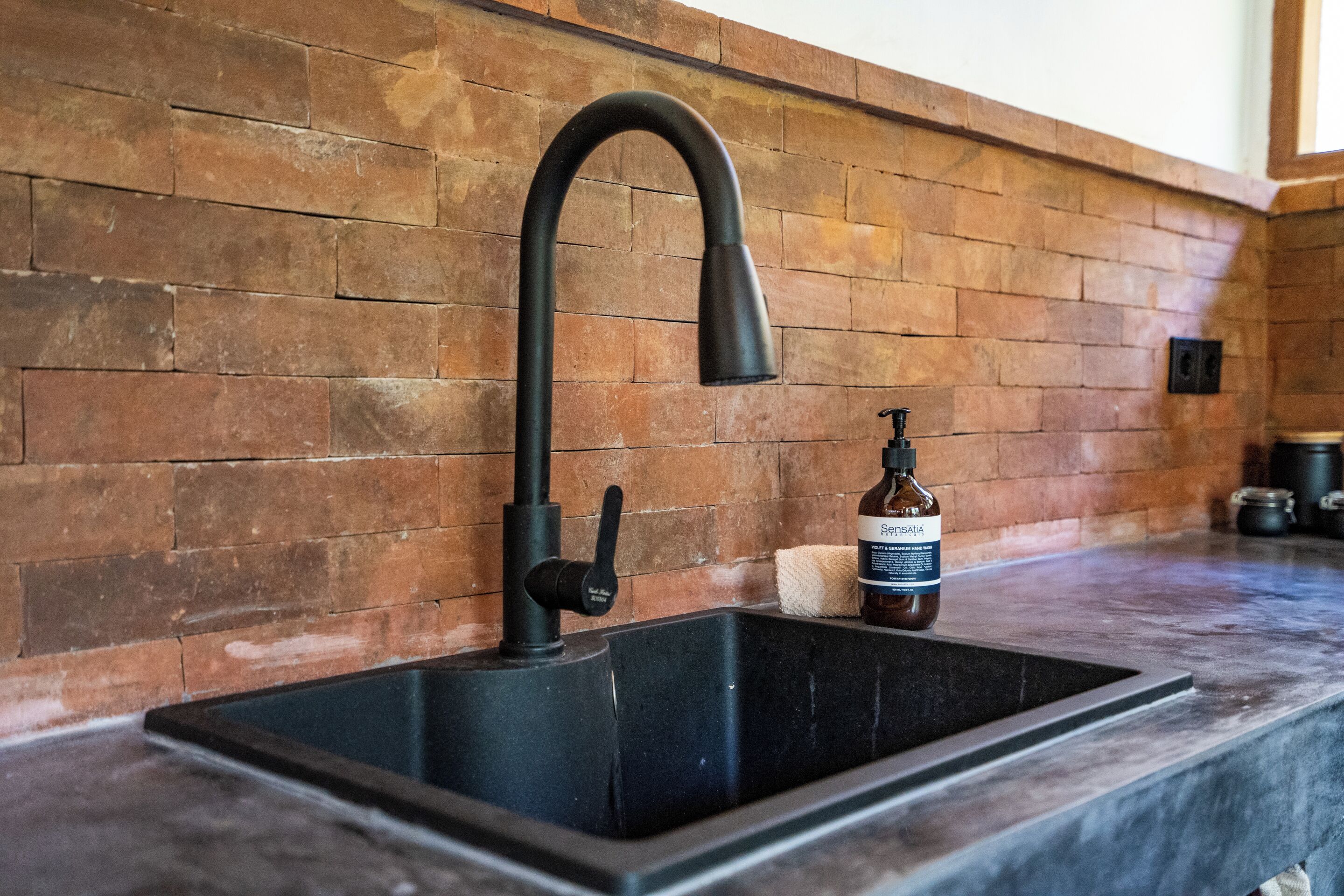 A kitchen with a black sink, a curved faucet, and a brick wall.